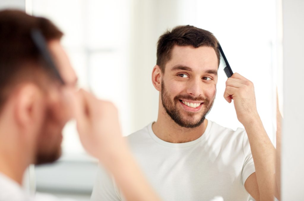 Smiling man with a mirror after hair treatment at The Skin and Hair Clinic.